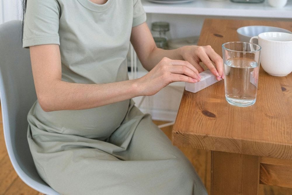 A pregnant woman preparing to take a supplement for pregnancy in a bright kitchen.